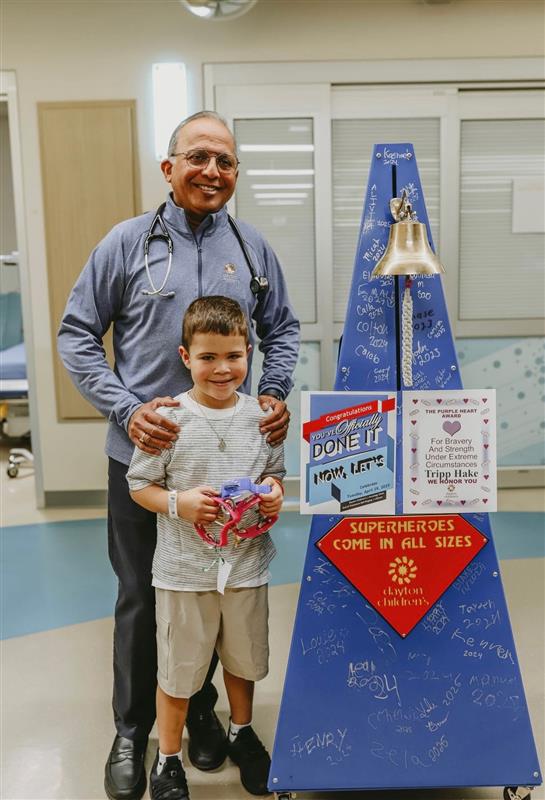 Tripp poses for a photo by the bell at Dayton Children's with Dr. Dole