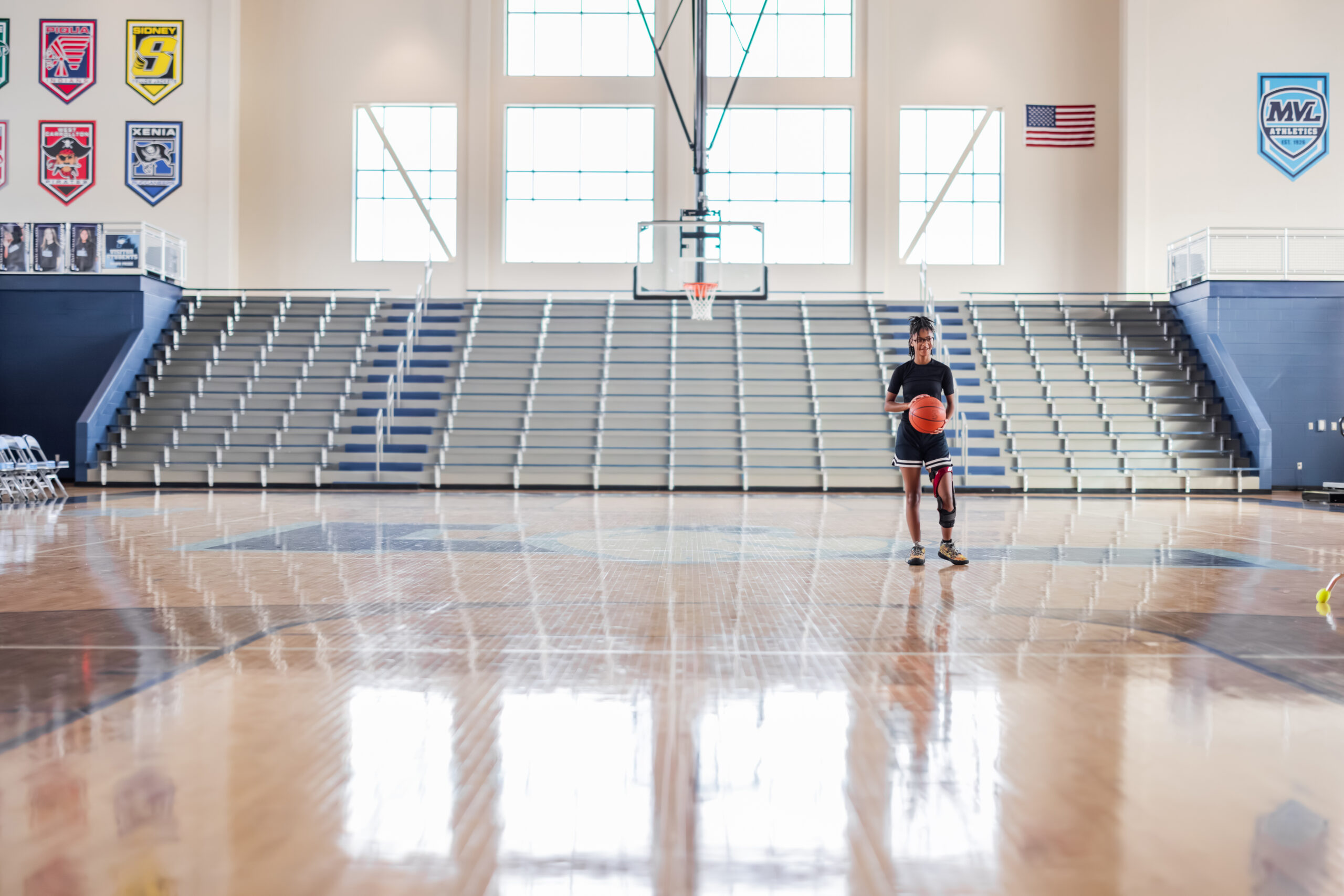A female teen basketball player holds a basketball in the middle of the court.