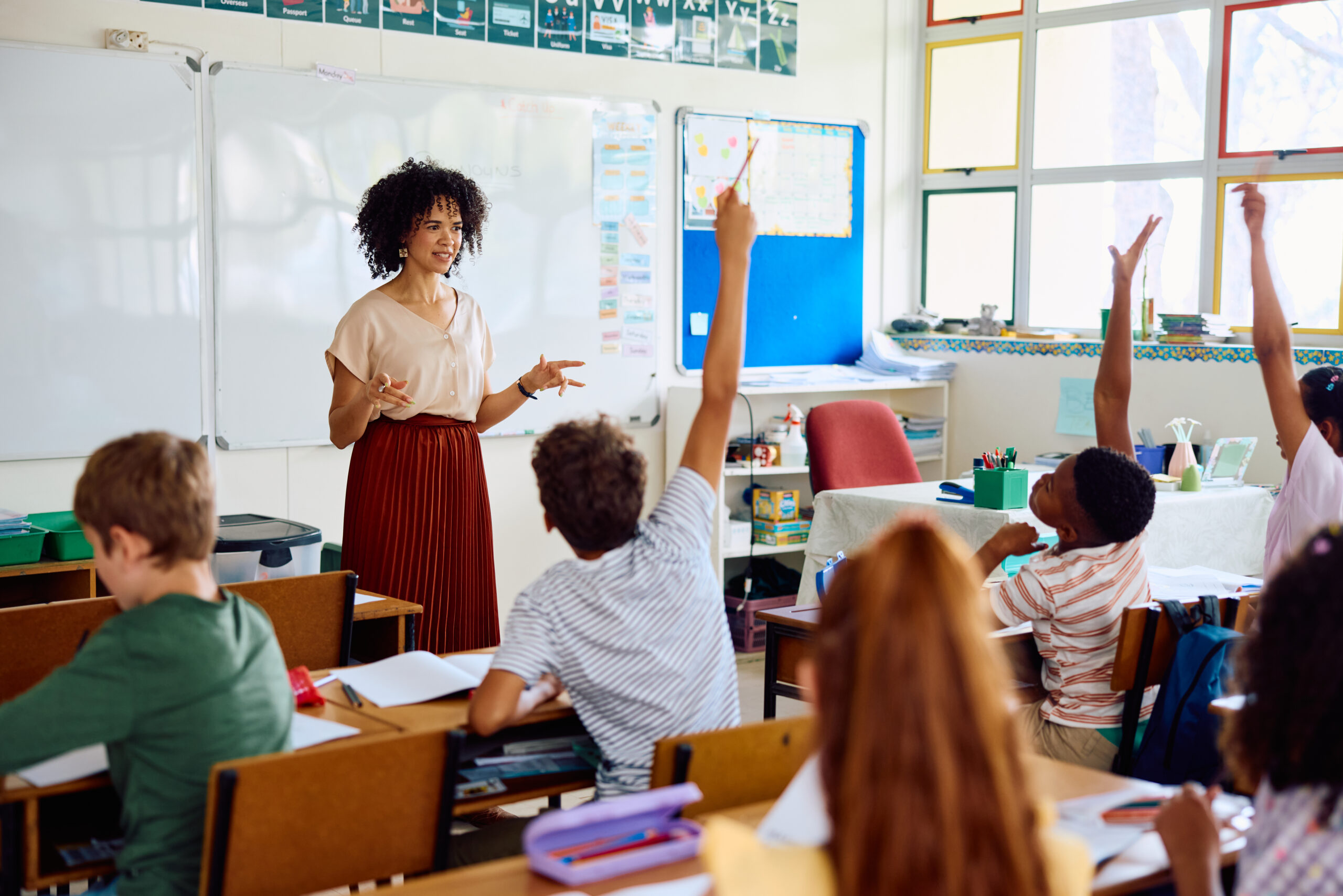 a teacher stands in front of a classroom full of students raising their hands